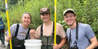 three students in waders with sampling equipment in stream
